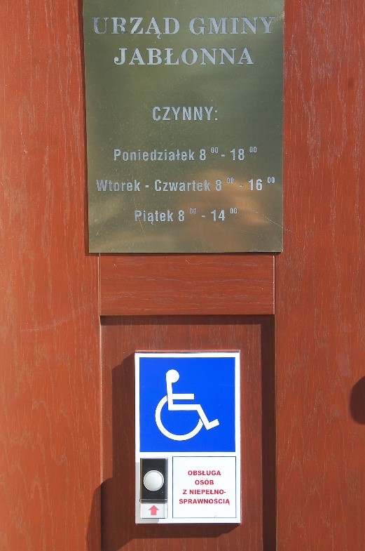 Drzwi Urzędu Gminy przedstawiające tablicę z godzinami pracy Urzędu oraz system obsługi osób z niepełnosprawnościami