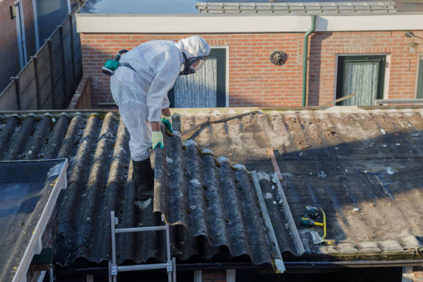 Mężczyzna ubrany w biały kombinezon ochronny usuwa azbest z dachu budynku